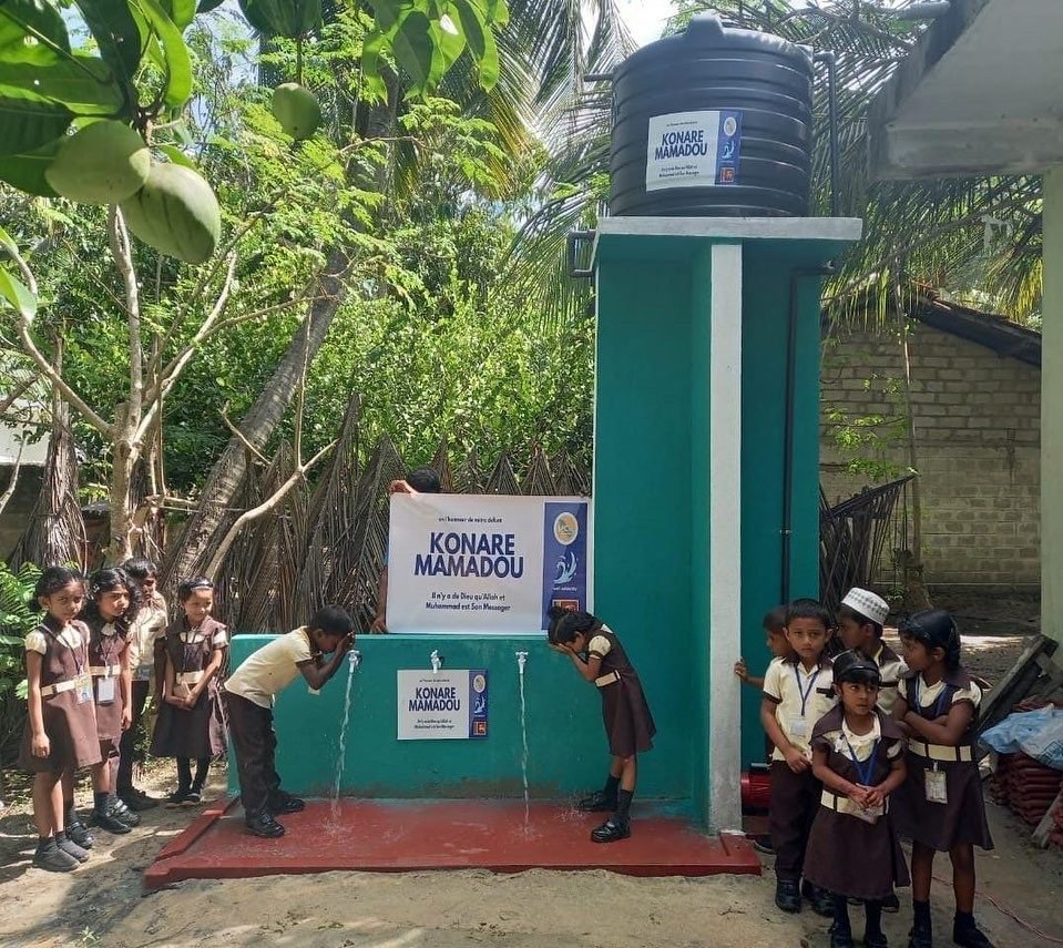 Community water well with a storage tank and several taps, children washing, built with Well Solidarity