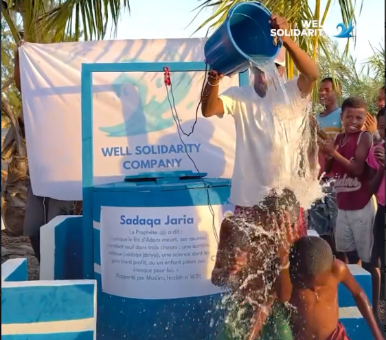 Bucket of water poured over a child at the inauguration of a classic well in Madagascar, plaque reading Sadaqa Jariya