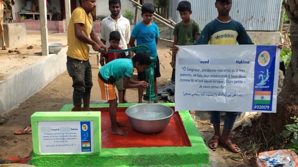 Boy drinking from a green hand pump while the village watches, plaque with a dua for parents