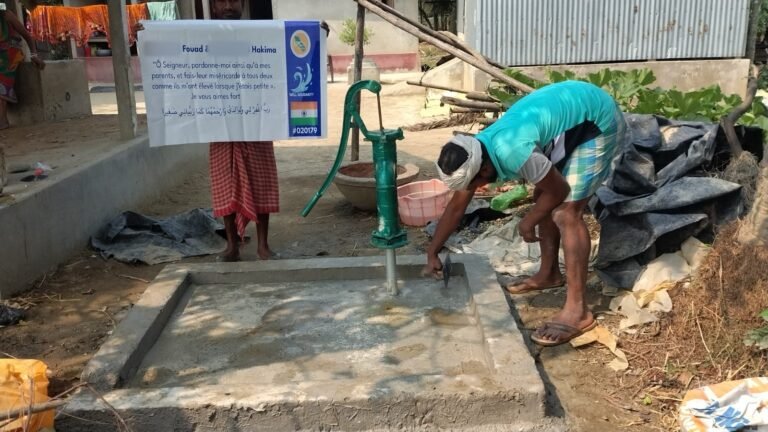 Worker finishing the concrete platform of a hand-pump well, with a plaque carrying a dua for the customer's parents